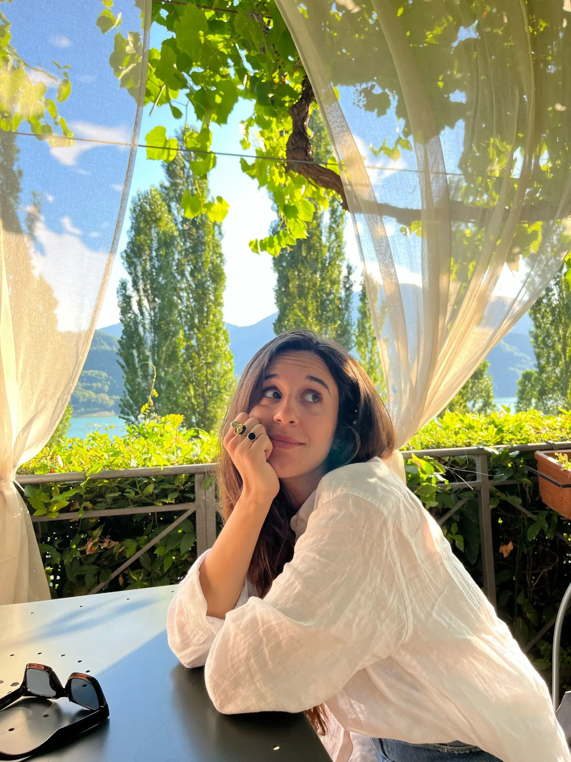 una ragazza mora seduta a un tavolo guarda verso l'alto. il braccio appoggiato al tavolo regge il mento.